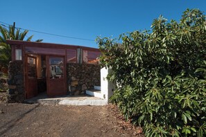 A rustic building with a stone wall entrance, a wooden door, and a white exterior.