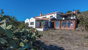 A white building with a red-tiled roof, a stone wall, and a cactus plant in the foreground. - Casas Rurales Herreñas (Valverde)