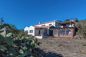 A white building with a red-tiled roof, a stone wall, and a cactus plant in the foreground.