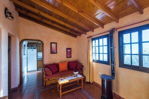 A cozy living room with a wooden ceiling, a sofa, a table, and a window with curtains. - Casas Rurales Herreñas (Valverde)