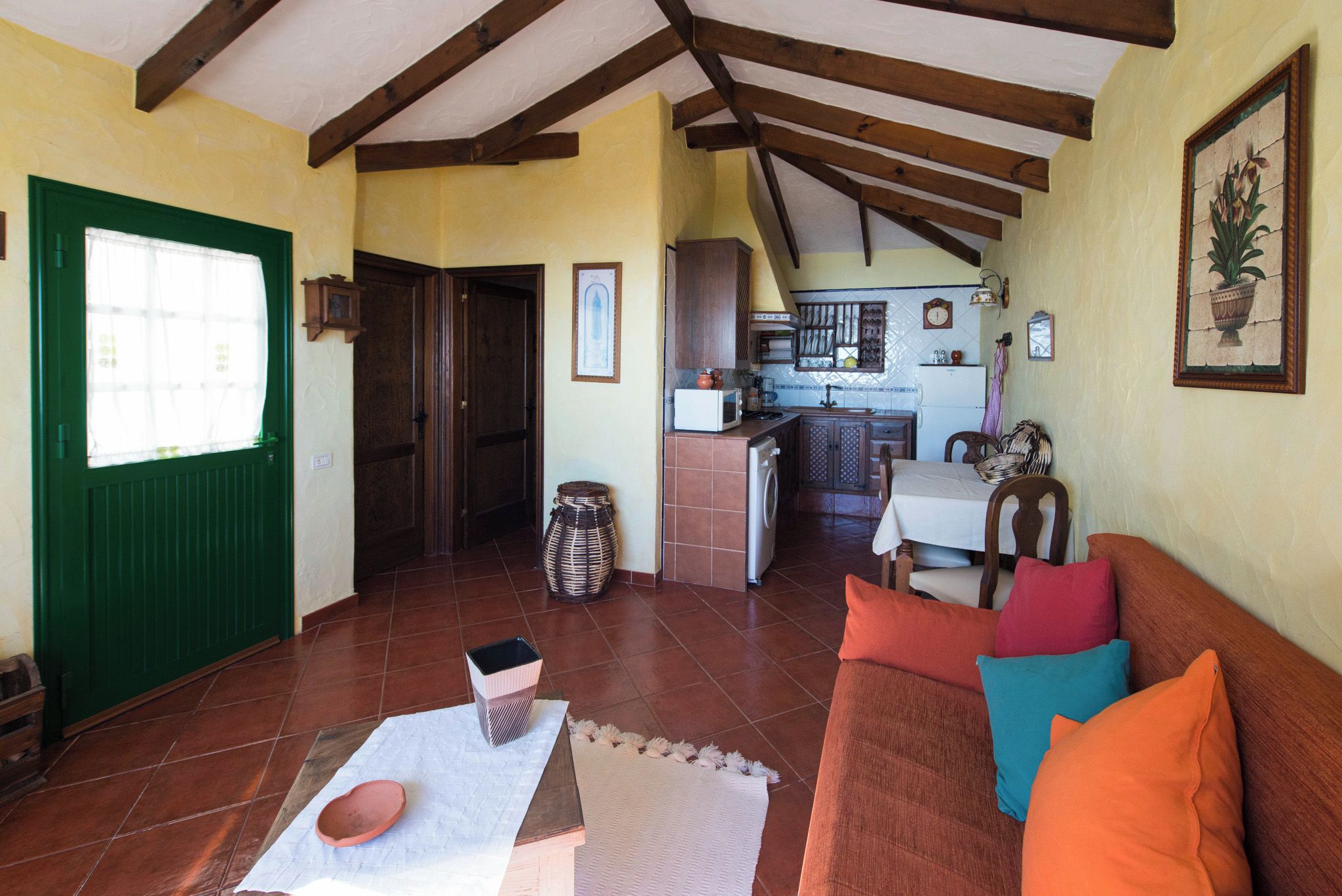 A cozy living room with a sofa, a dining table, and a kitchen in the background.