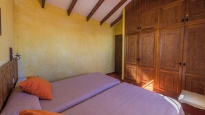A room with two beds, wooden wardrobe, and a window allowing natural light.