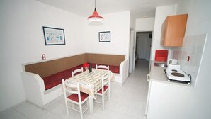 Una cocina pequeña y luminosa con armarios blancos, una lámpara colgante roja y un comedor con mesa y sillas.