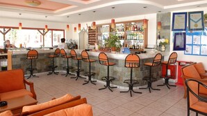 Una zona de bar con mostrador, varios taburetes altos y un área de estar con sillas anaranjadas.