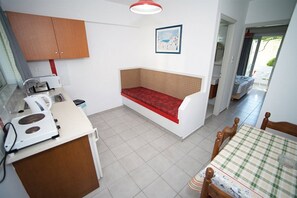 Cocina compacta con un banco incorporado, una mesa de comedor con mantel a cuadros y vistas al exterior a través de una puerta.
