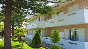 Un moderno edificio de apartamentos de dos pisos con fachada blanca, balcones y un jardín cuidado con árboles y arbustos.