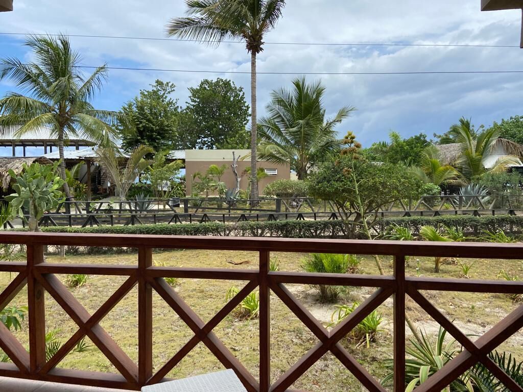 A view from a balcony with a wooden railing, overlooking a landscaped area with palm trees and a building in the background.