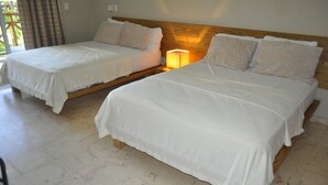 A room with two beds, each with white bedding and patterned pillows. There is a nightstand with a lamp between the beds. - Paradise Island Beach Resort (Punta Rucia)