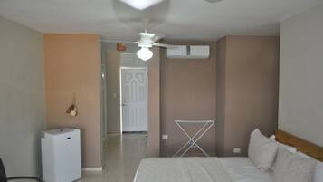 Quarto com cama, ventilador de teto, ar condicionado, varal e um pequeno eletrodoméstico branco.