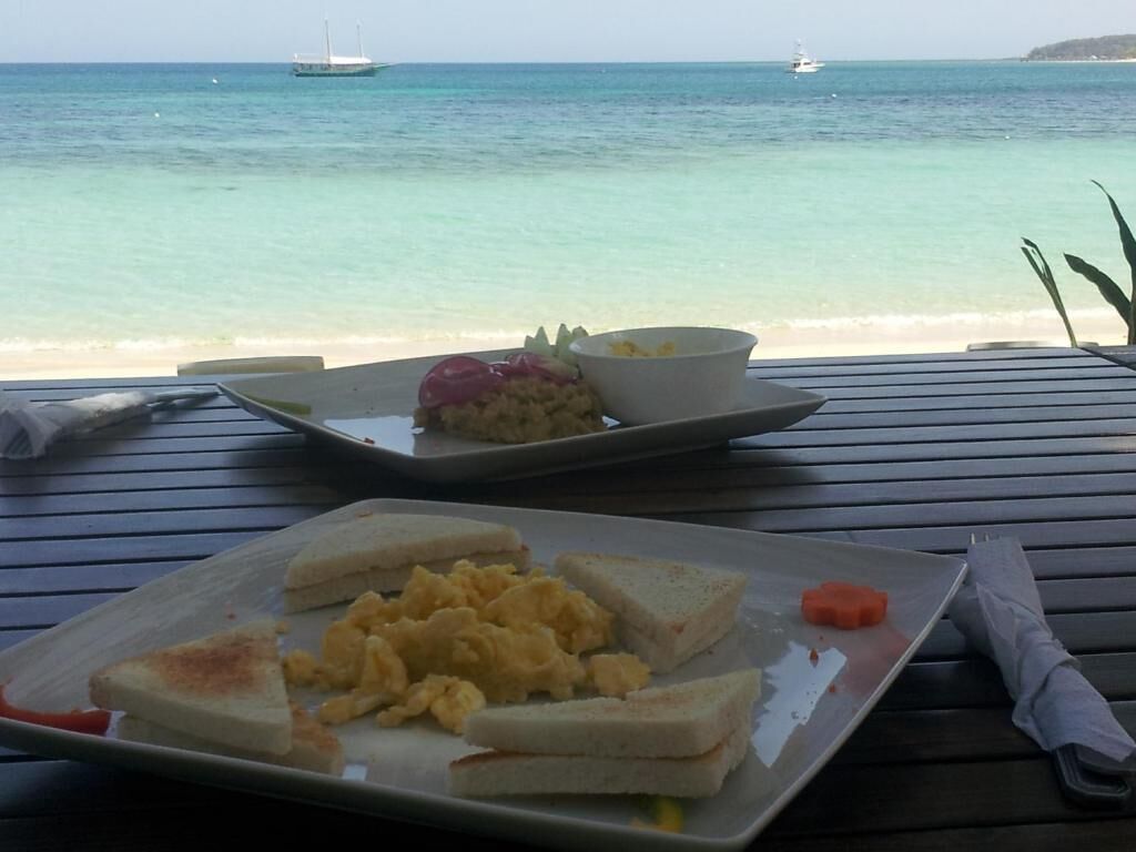 Comida sobre una mesa de madera con vista al mar y barcos al fondo.