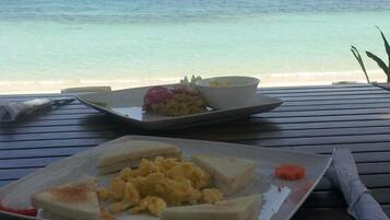 Comida sobre una mesa de madera con vista al mar y barcos al fondo.