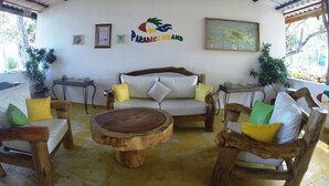 A cozy room with a wooden sofa, round wooden table, and potted plants. A sign on the wall reads "Paradise Island." - Paradise Island Beach Resort (Punta Rucia)