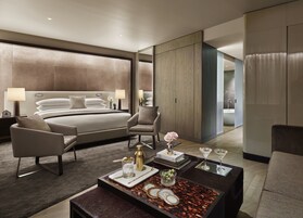 Quarto de hotel moderno com uma cama grande, duas poltronas, uma mesa de centro com amenidades e vista para o banheiro.