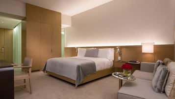 A hotel room with a bed, a desk, a chair, a sofa, and a small table with a vase of flowers.