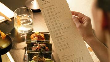 A person holding a menu with various dishes listed, a glass of water, and a candle on a table.