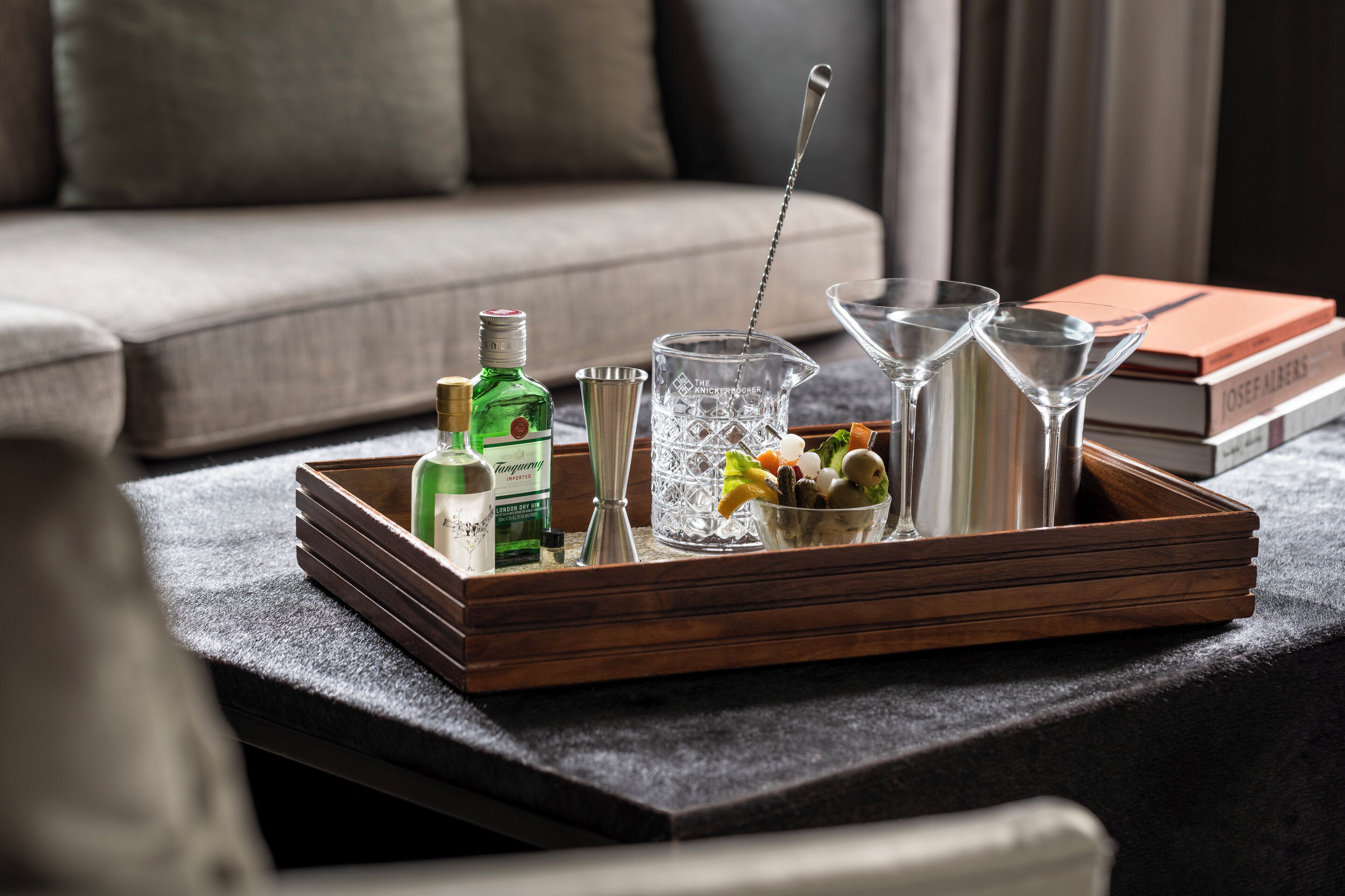 A tray with a bottle, a martini glass, a cocktail shaker, and a bowl of fruit on a table.