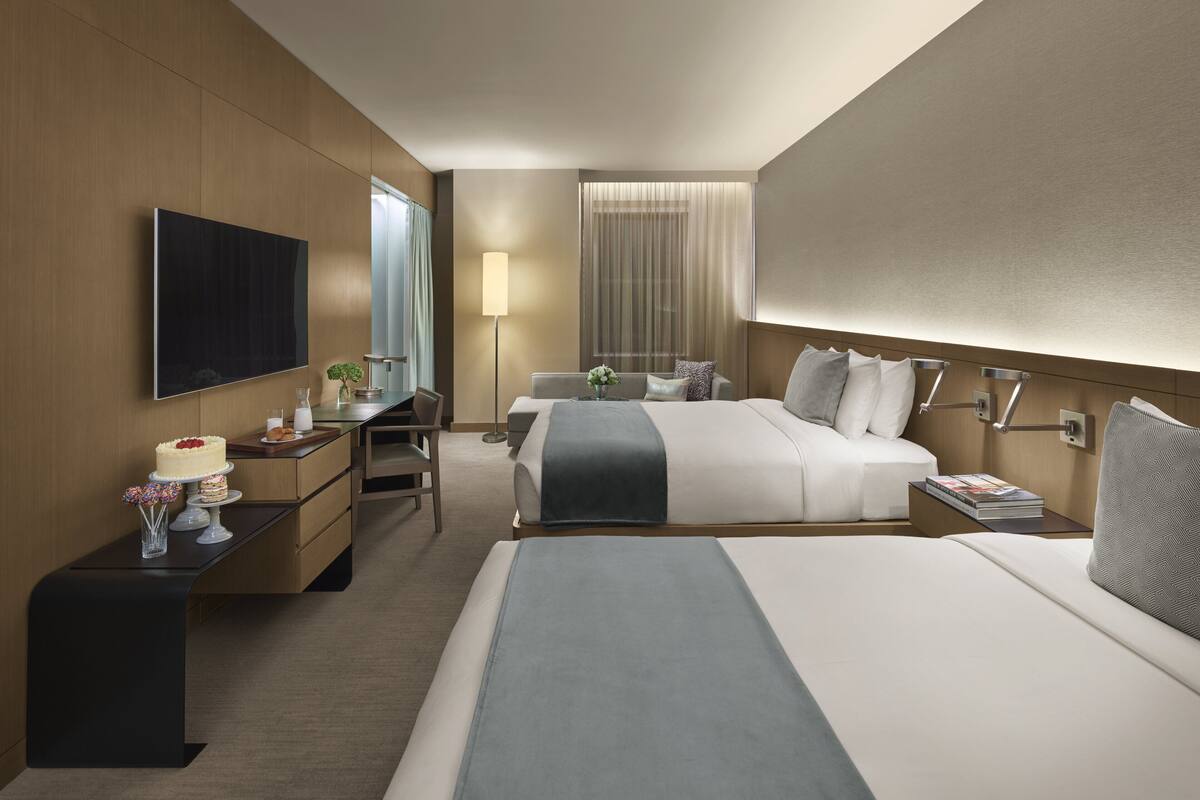 Habitación de hotel con una cama grande, un escritorio, una silla, un televisor y una mesita de noche con lámpara.