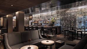 A modern bar area with a marble countertop, leather seating, and a wall of wine bottles.