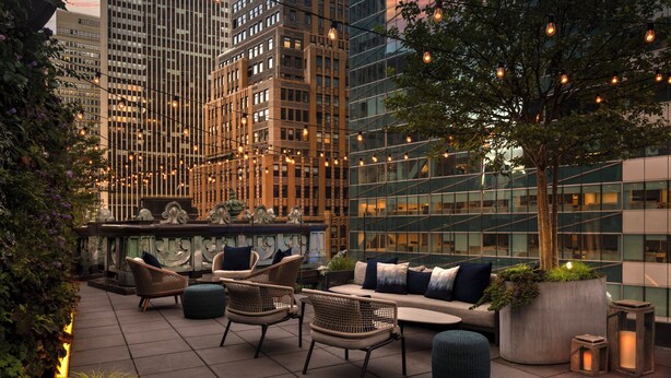 A rooftop terrace with wicker furniture, a bar area, and a view of tall buildings.