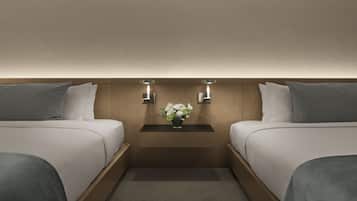 A hotel room with two beds, a nightstand with a vase of flowers, and wall-mounted lights.