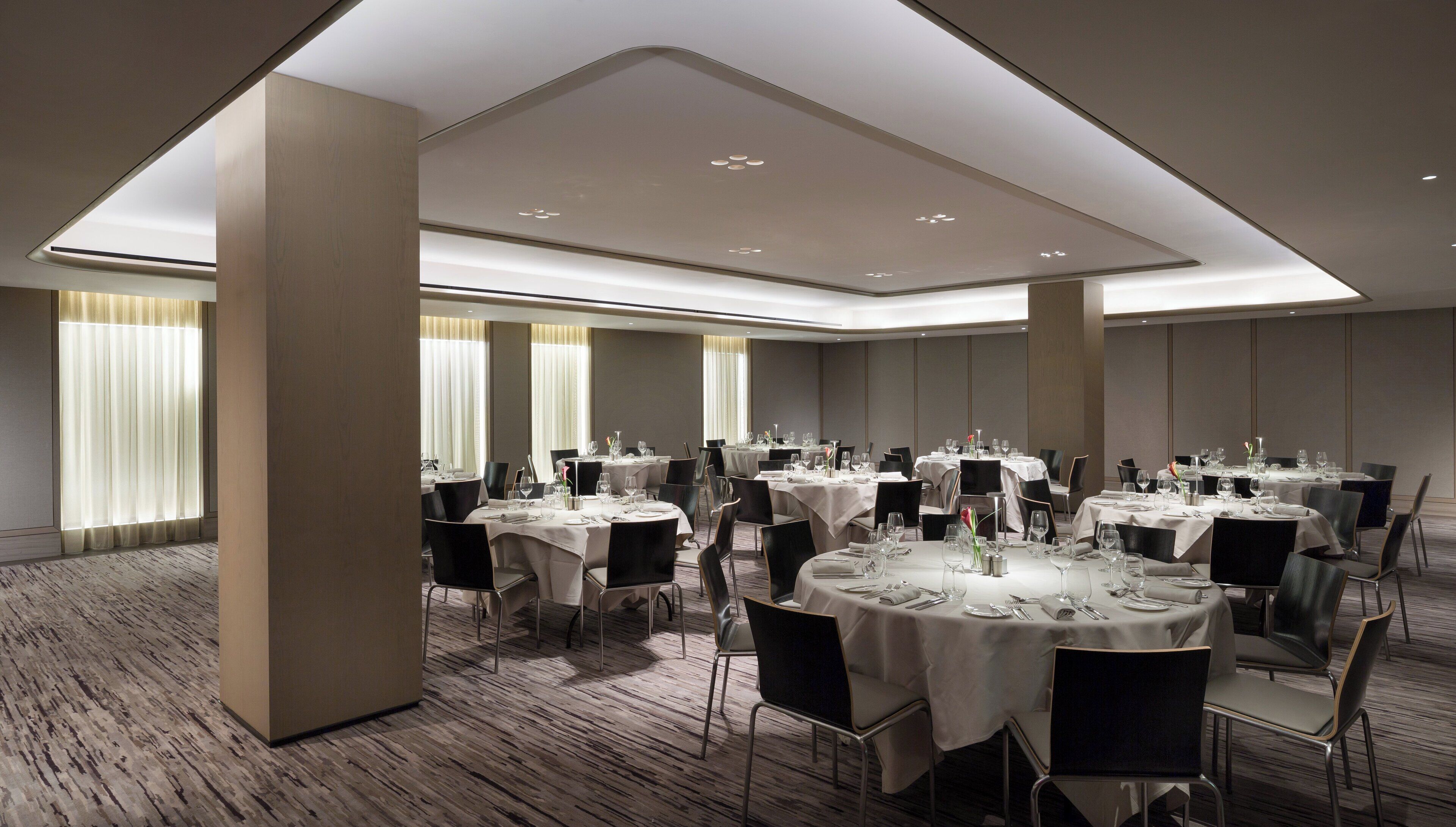 A conference room with multiple tables set for dining, featuring a modern design with neutral tones and ample lighting.