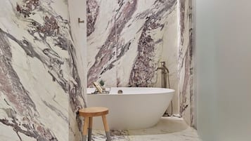 A bathroom with a freestanding bathtub, a wooden stool, and marble walls.