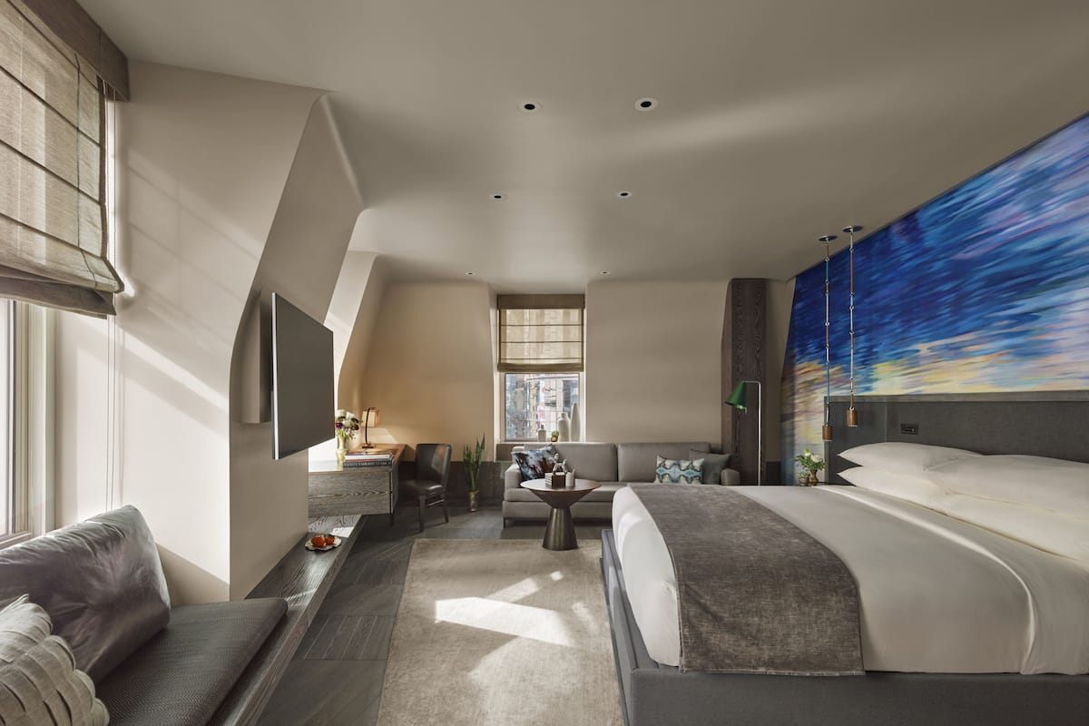 Una habitación de hotel moderna con una cama grande, un sofá, un escritorio y vistas a la ciudad desde la ventana.