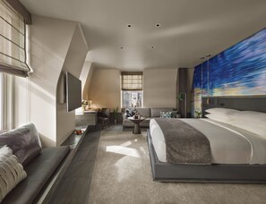 A modern hotel room with a large bed, a sofa, a desk, and a view of the city through the window.