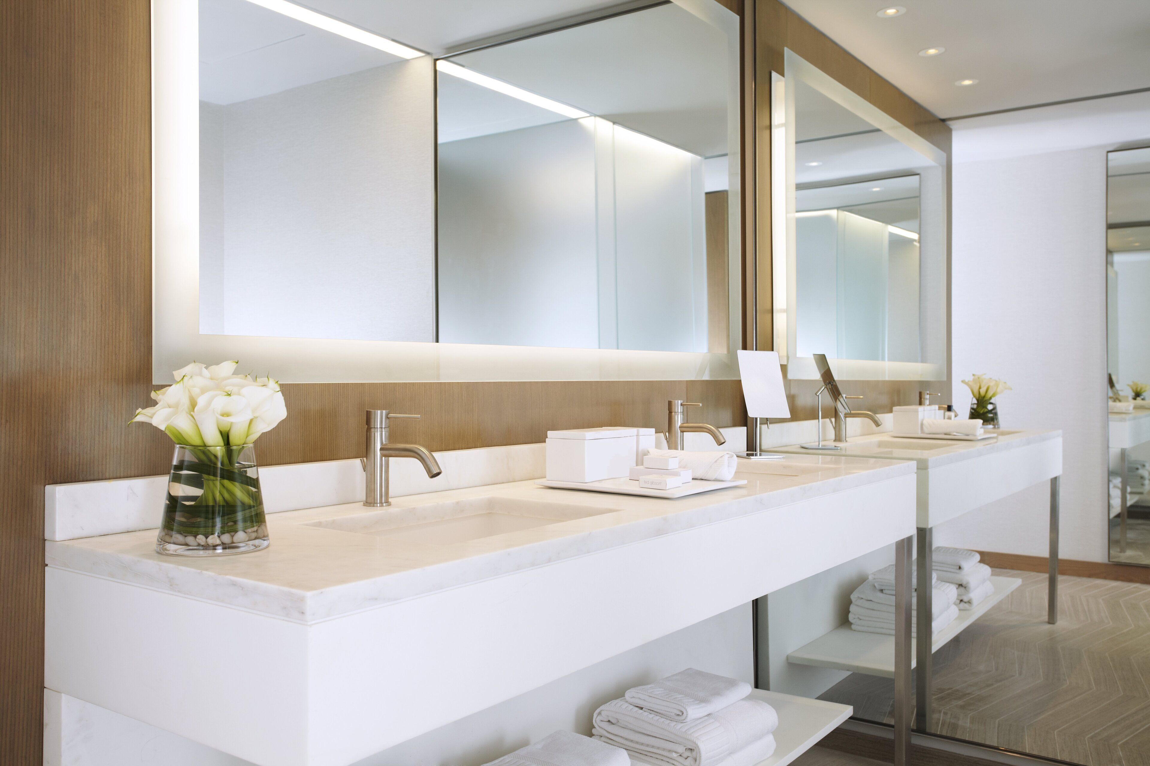 A modern bathroom with a long vanity, two sinks, a large mirror, and a vase of flowers.