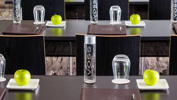 Une salle de conférence avec des tables préparées pour des réunions, chacune étant équipée d’un ordinateur portable, d’un verre d’eau et d’une pomme verte.