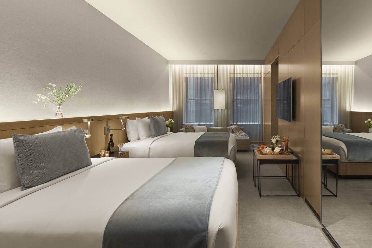 Habitación de hotel con dos camas, una mesita con un florero y un televisor en la pared.