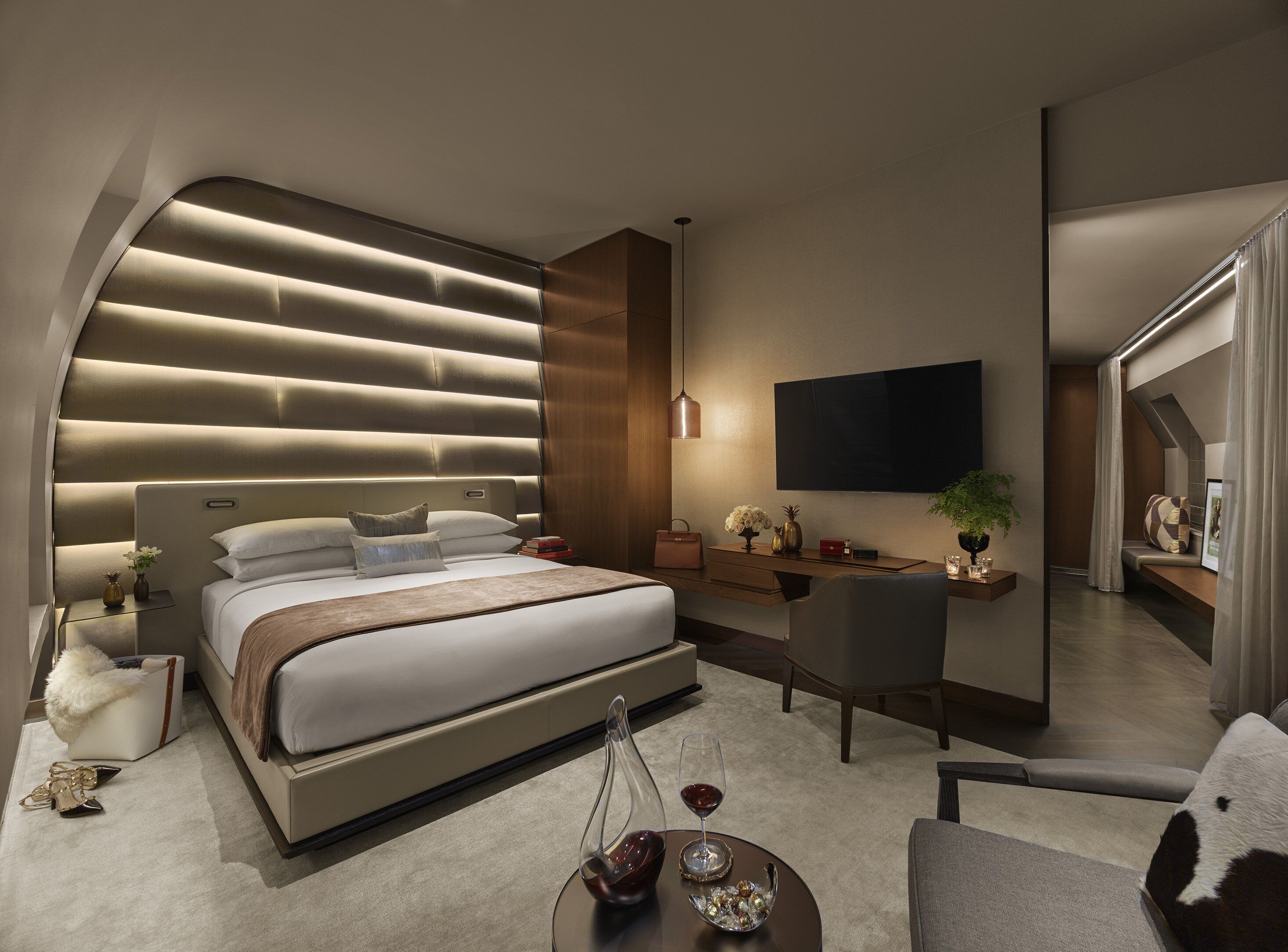 A modern hotel room with a large bed, a desk, a chair, and a TV mounted on the wall.