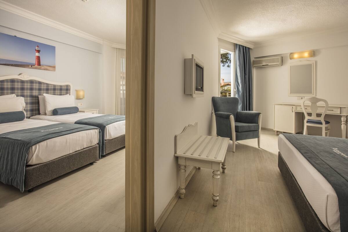 Une chambre d’hôtel avec deux lits, un bureau, une chaise, une petite table, un téléviseur et un tableau représentant un phare.