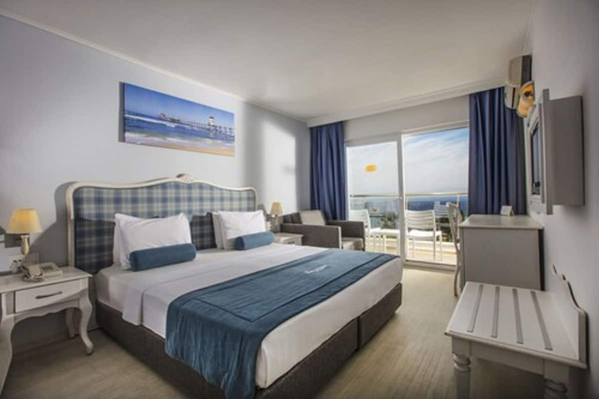 Une chambre d’hôtel avec un grand lit, un bureau, une chaise, une télévision et un balcon avec vue.