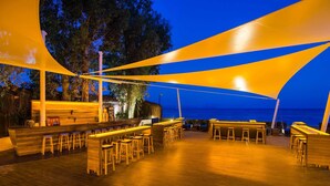 Un área de bar al aire libre con muebles de madera y vista al océano al anochecer.