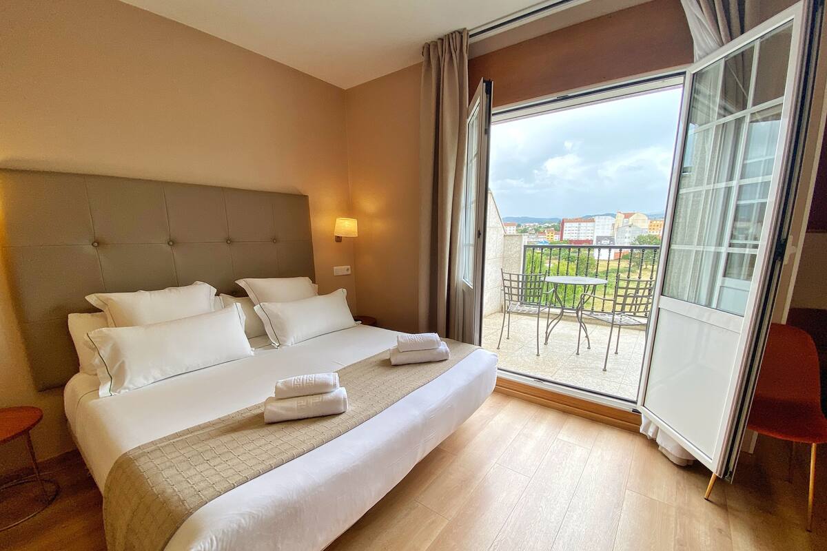 A hotel room with a large bed, a balcony with a table and chairs, and a view of buildings.