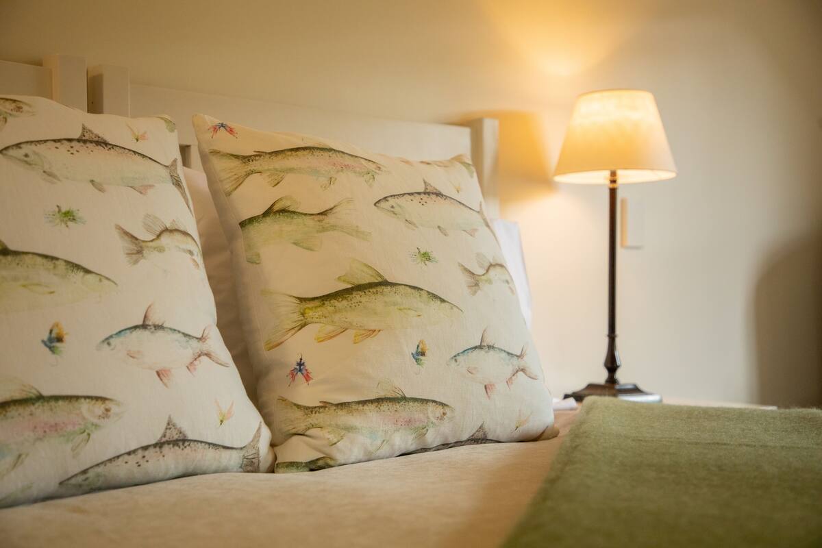 A bed with two pillows featuring a fish pattern, a bedside lamp, and a green throw blanket.