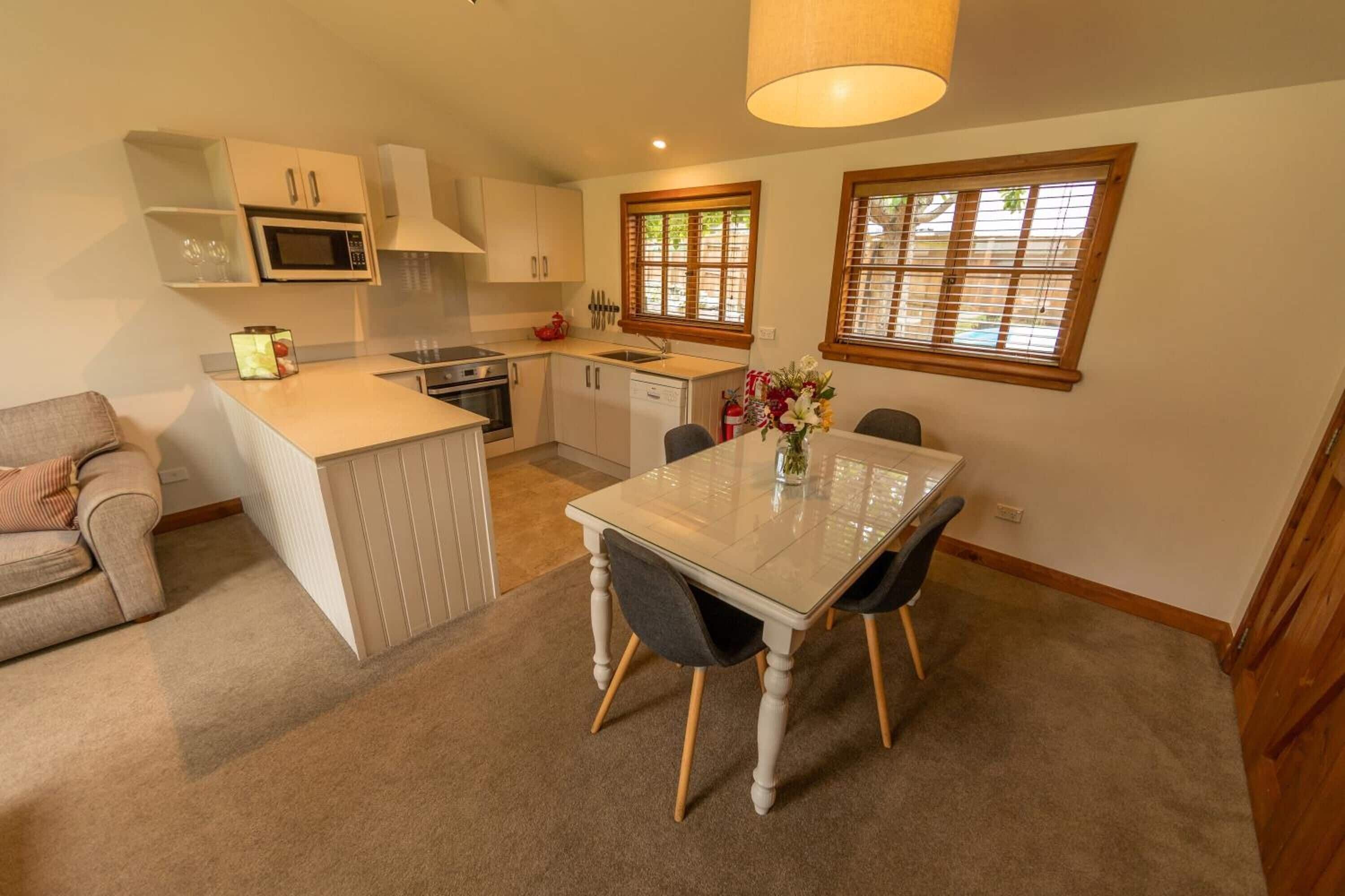 A compact kitchen with a dining area, a microwave, a sink, and a window with blinds.