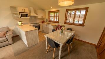 A compact kitchen with a dining area, a microwave, a sink, and a window with blinds.