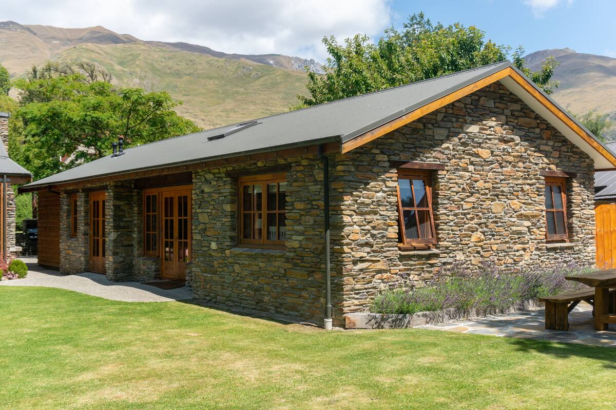 A stone house with a sloped roof, wooden doors, and windows.