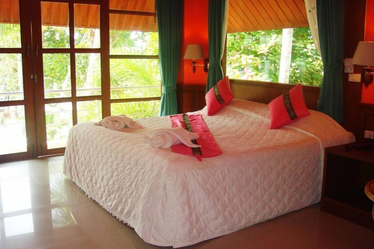 A large bed with a quilted white duvet, two pillows, and a folded towel on it.