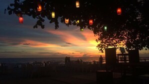 Vista al atardecer con una playa y un árbol decorado con faroles colgantes.