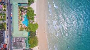 Vista aérea de una playa con piscina, palmeras y una carretera con vehículos.