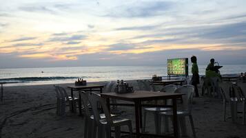 Ein Restaurant direkt am Strand mit Tischen, Stühlen und einer Speisekarte, mit Blick aufs Meer.