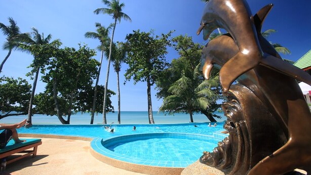 Una piscina con una escultura de delfín, rodeada de palmeras y un cielo azul despejado.