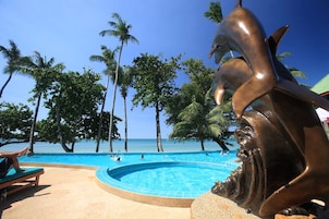Ein Swimmingpool mit einer Delfin-Skulptur, umgeben von Palmen und blauem Himmel.