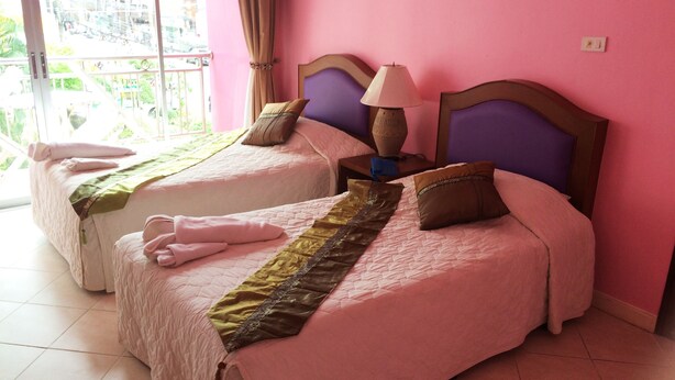 A hotel room with two beds, each with a headboard, pillows, and a bedside lamp. The room has a pink wall and a window with curtains. - Cookies Hotel (Ko Chang)