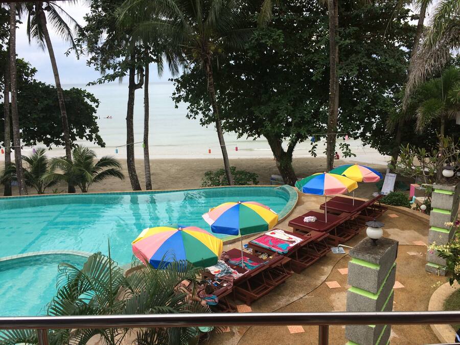Uma área de piscina com vários guarda-sóis coloridos, espreguiçadeiras e vista para a praia.