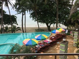 Zona de piscina con varios sombrillas de colores, sillas de descanso y vista a la playa.