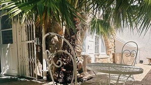 Un patio con mesa y sillas de metal, rodeado de baldosas de piedra y palmeras.